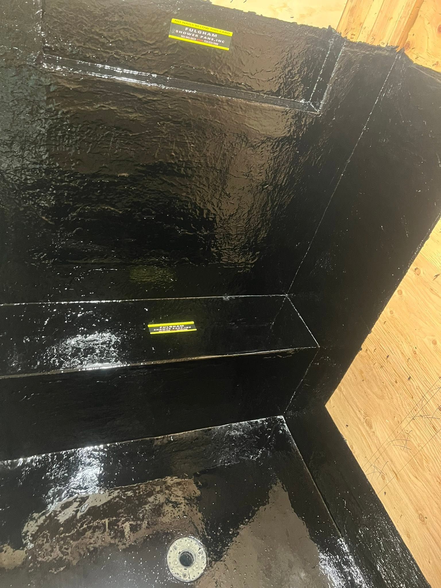 Black waterproof-lined corner with a wet floor and a small drain or plug hole near the bottom.