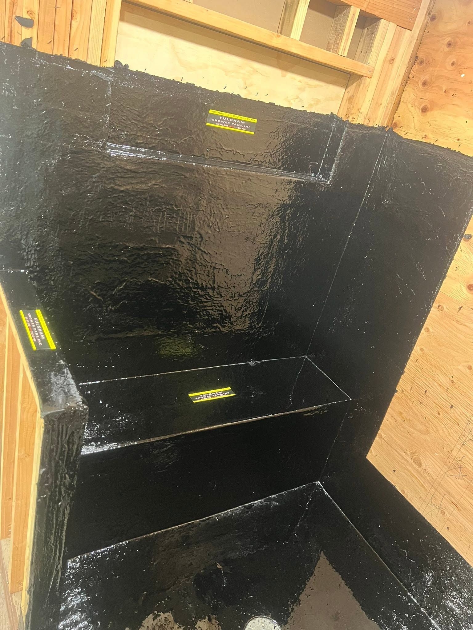 Black wooden steps with yellow safety labels inside a construction area with exposed plywood walls.