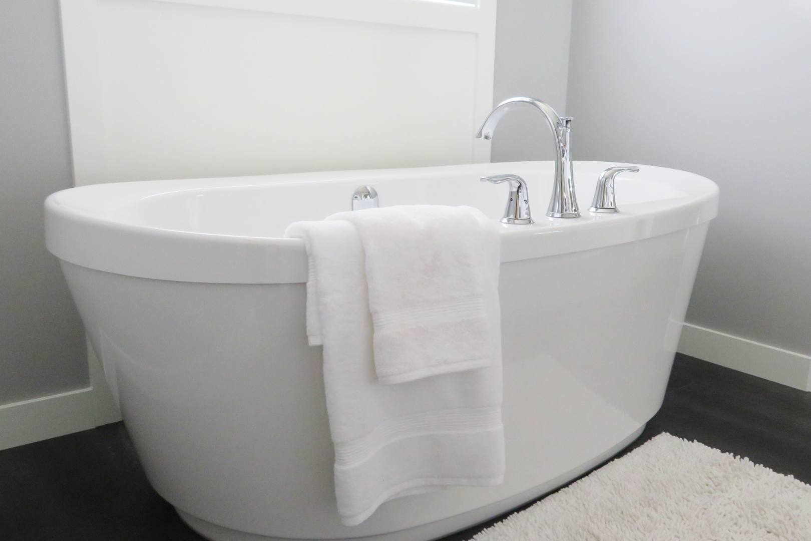 Modern white freestanding bathtub with chrome faucet and white towels in a bright bathroom