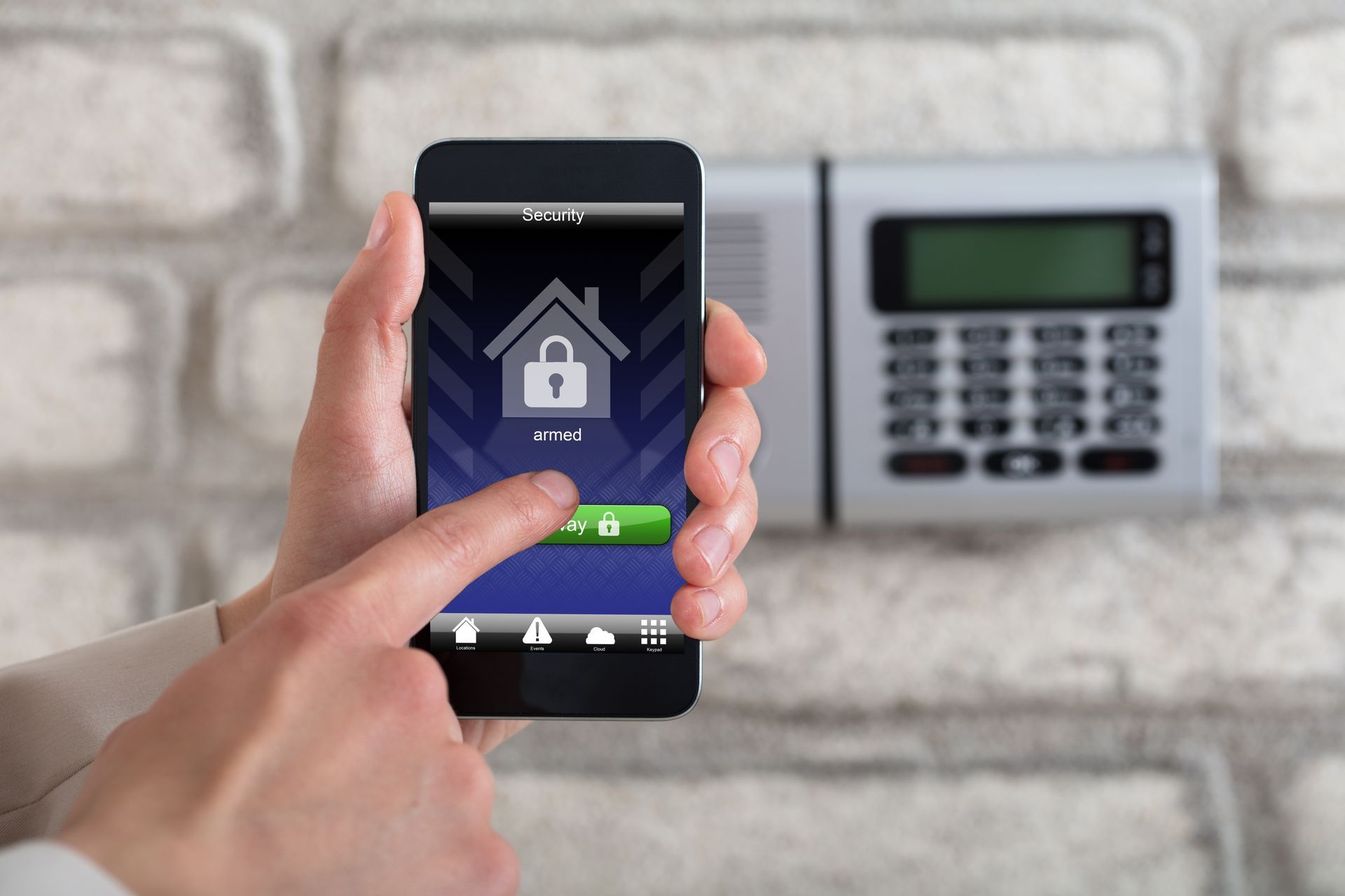 A person is holding a smart phone in front of a security system.