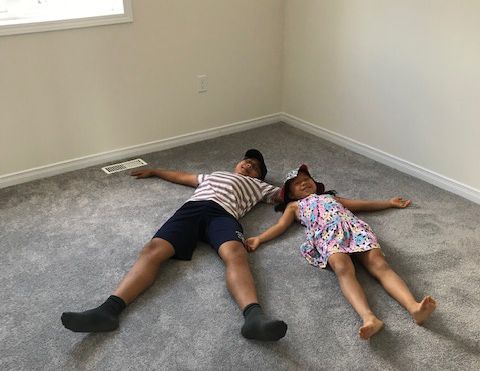 Two people lie on gray carpet, arms outstretched.