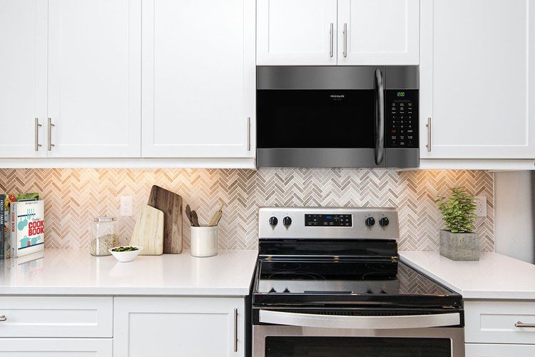 A kitchen with a stove , oven , microwave and white cabinets.
