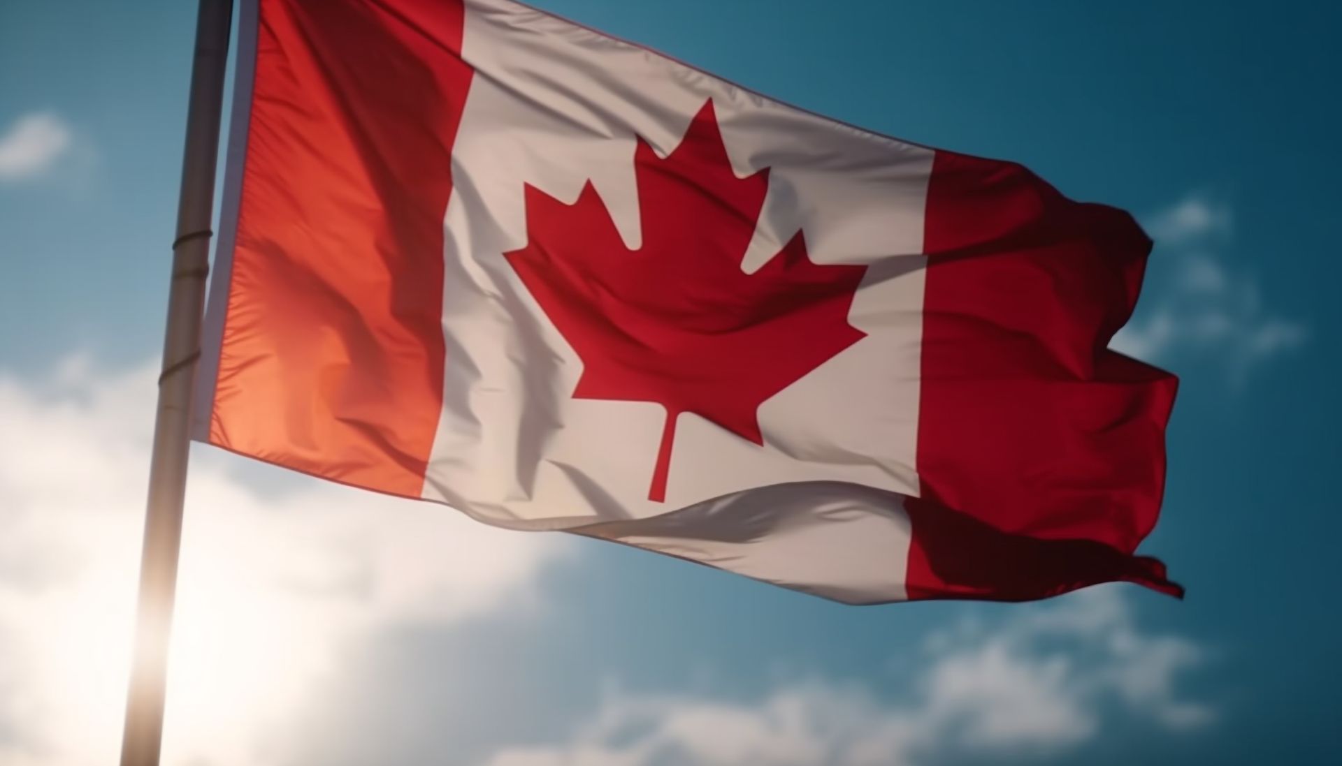 A canadian flag is waving in the wind against a blue sky.
