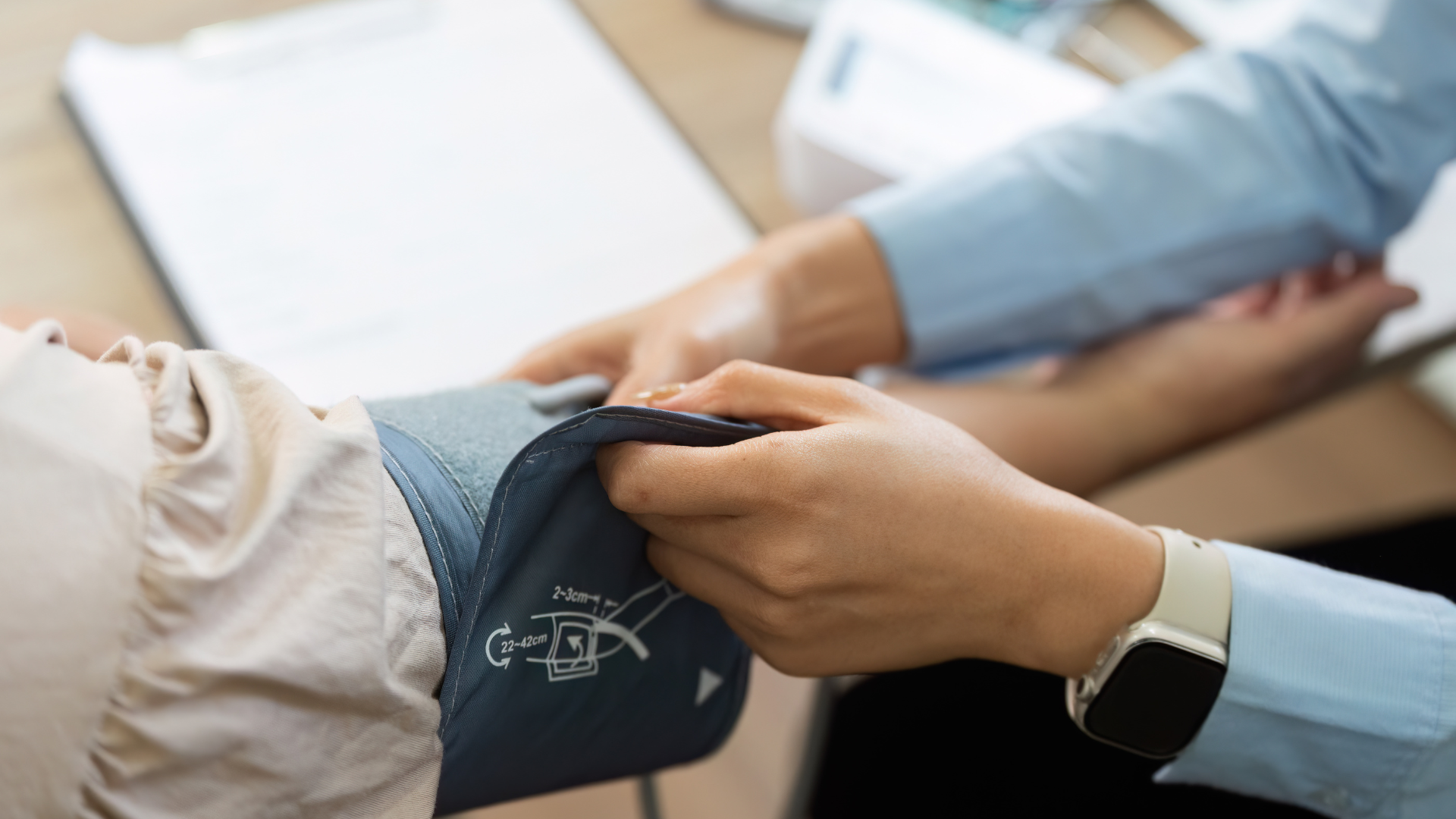 Person's arm has blood pressure cuff wrapped around it as another person checks the pressure in a medical setting.