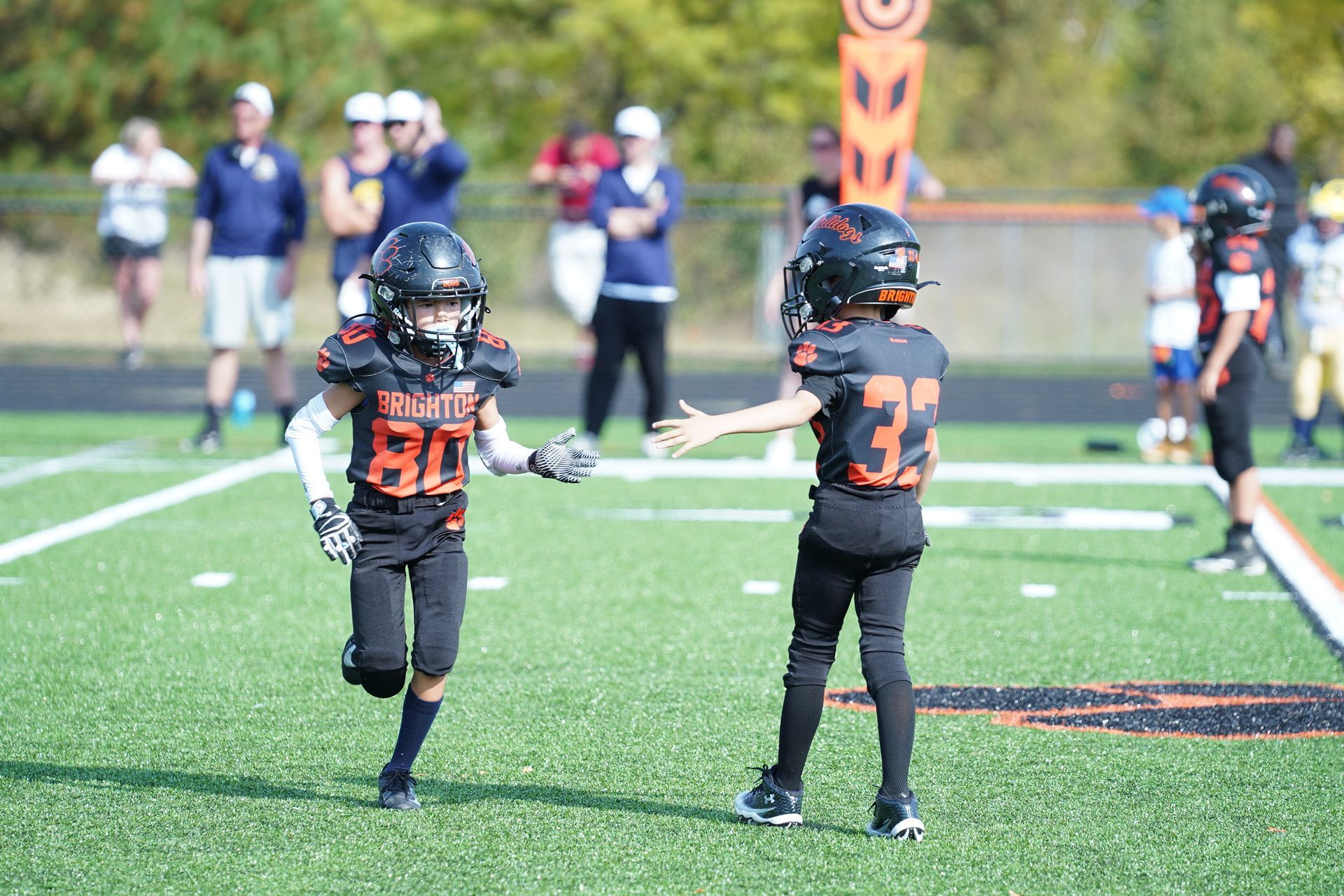 Four women in matching black event shirts pose on a football field with a crowd behind them.