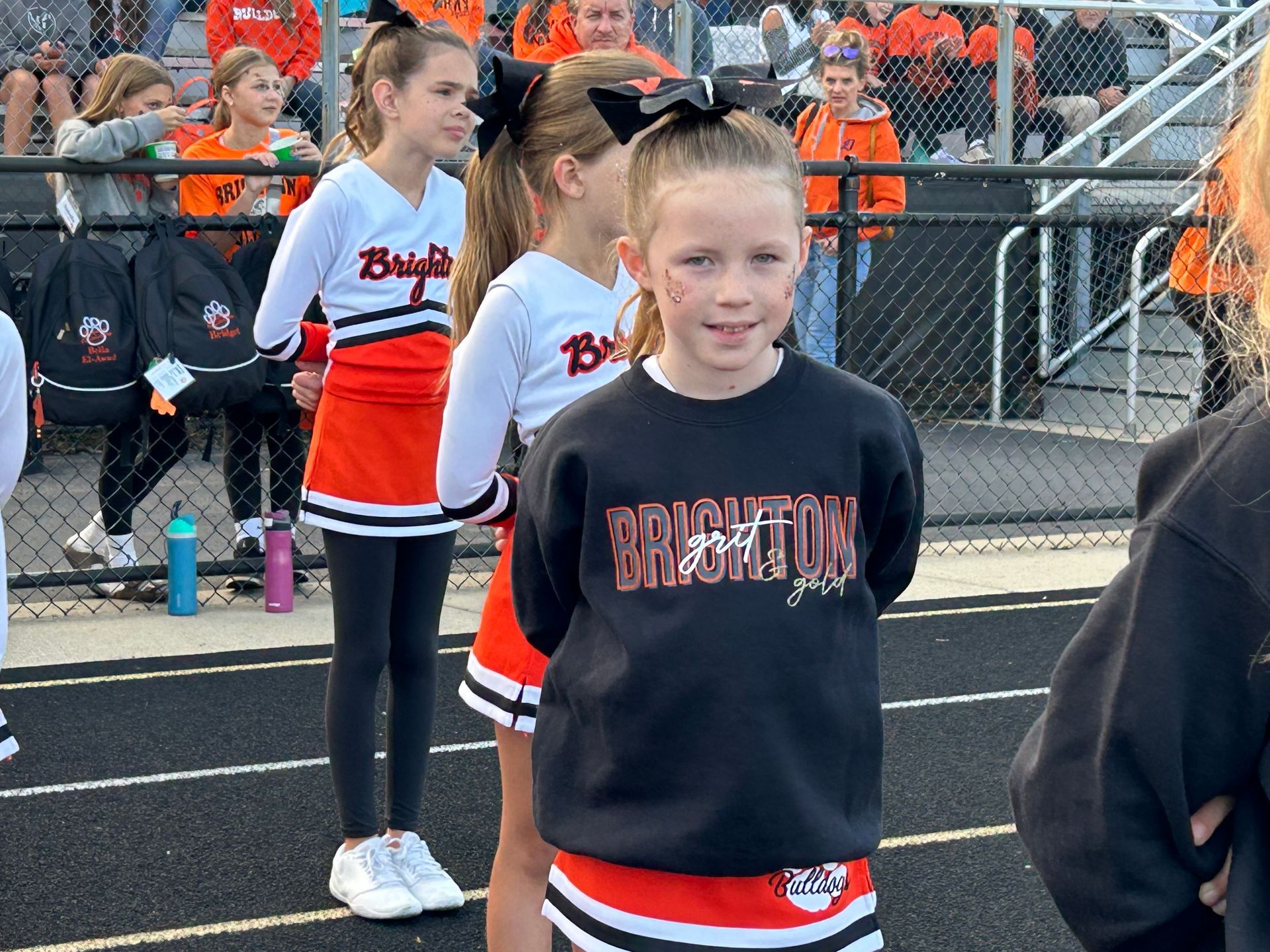 Cheerleading team posing on a football field at dusk, in red and black uniforms with pom-poms