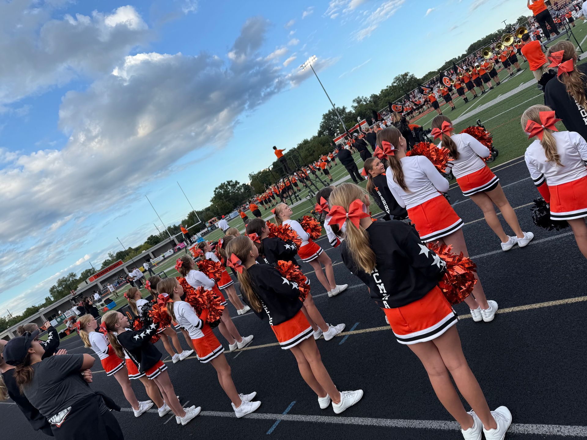 Cheerleaders in orange and black uniforms performing on a blue track field at a sports stadium