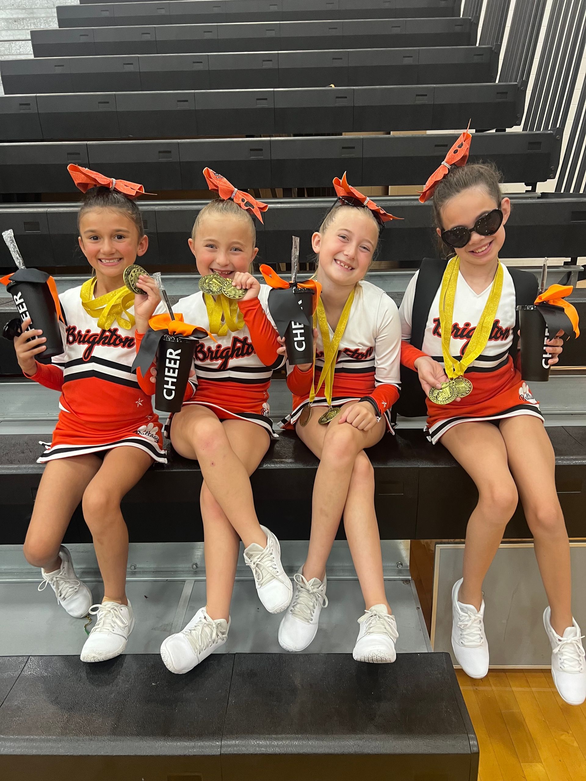 Cheerleading team in black and red uniforms posing on a gym floor with coaches behind them