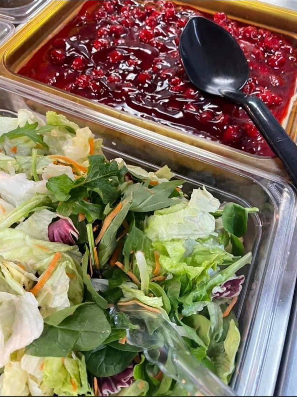 Salad bar with mixed green salad and a red berry dish in stainless steel trays, with a serving spoon.