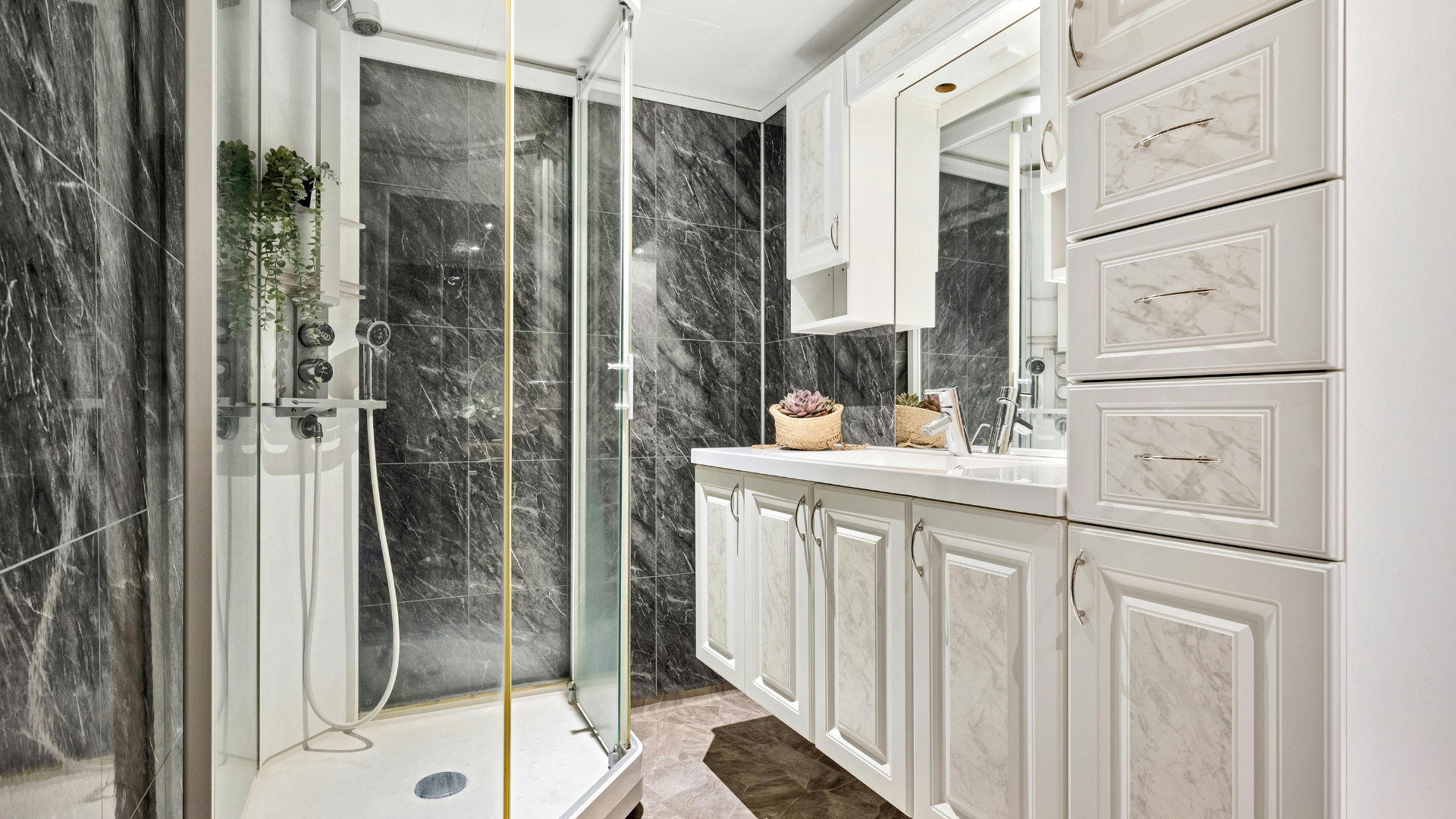 Modern bathroom with glass shower, gray marble tiles, and white vanity cabinets