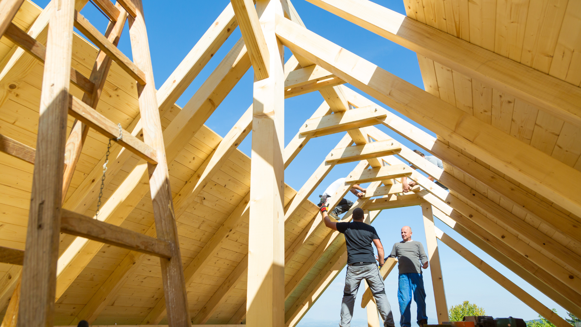 Construction workers framing a wooden roof with exposed beams at a house under construction