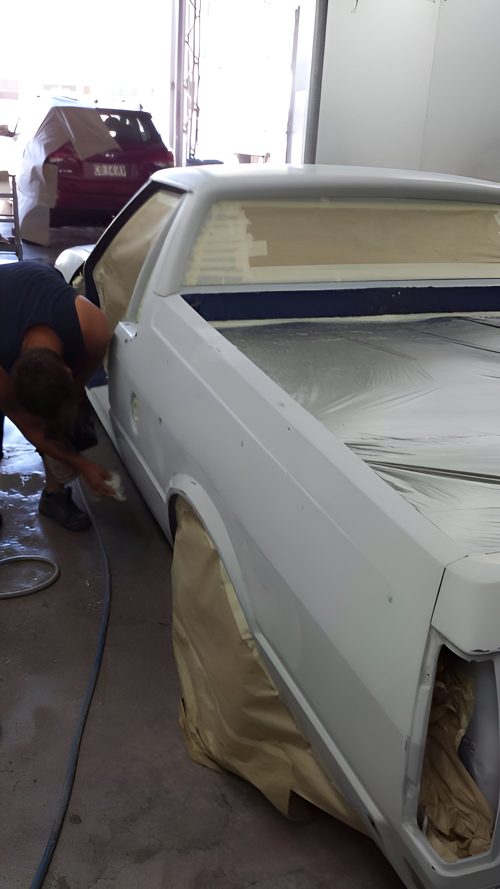 A Man Is Painting A White Car In A Garage — P & V Panel Works In Alice Springs, NT