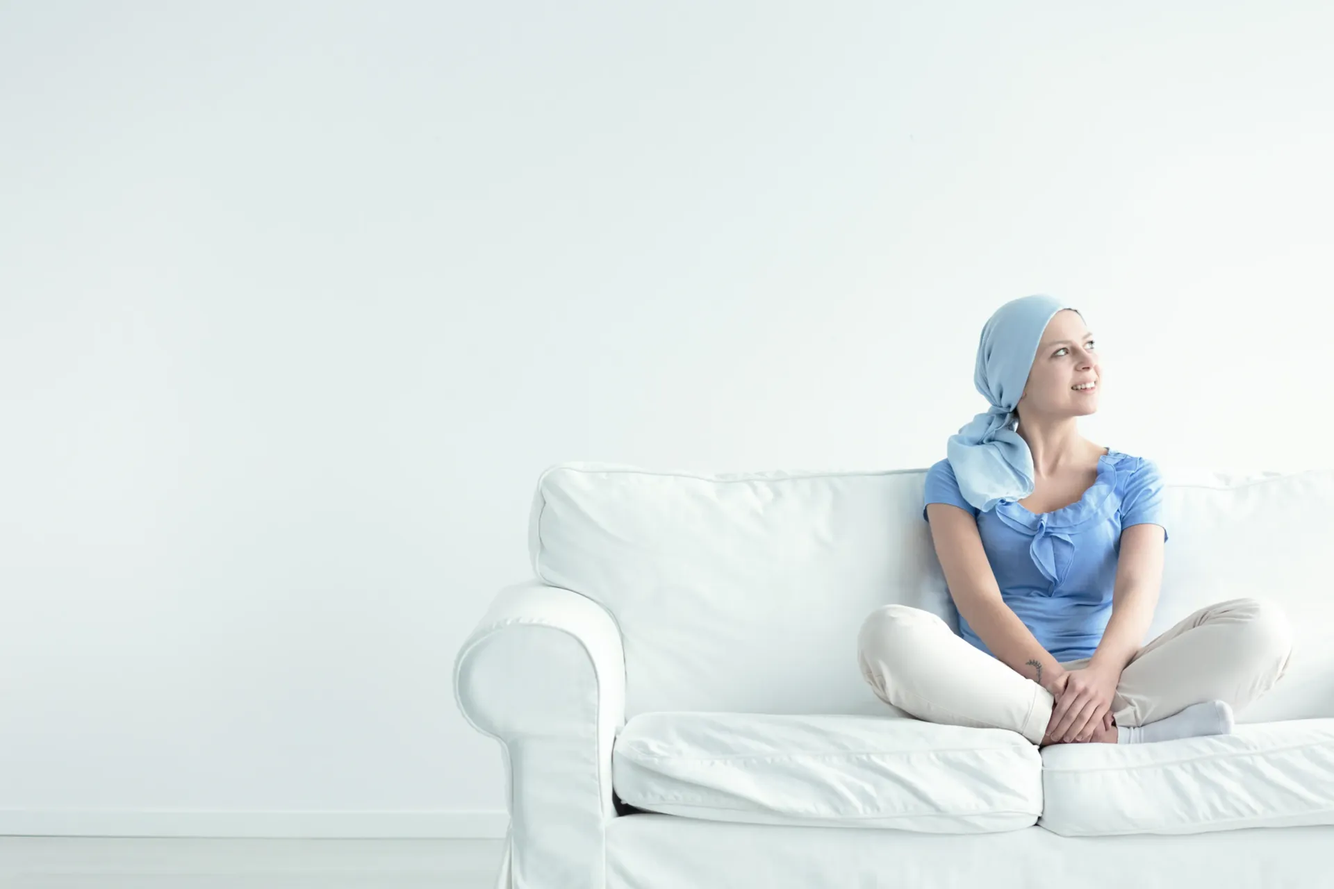 A woman with cancer is sitting on a white couch.