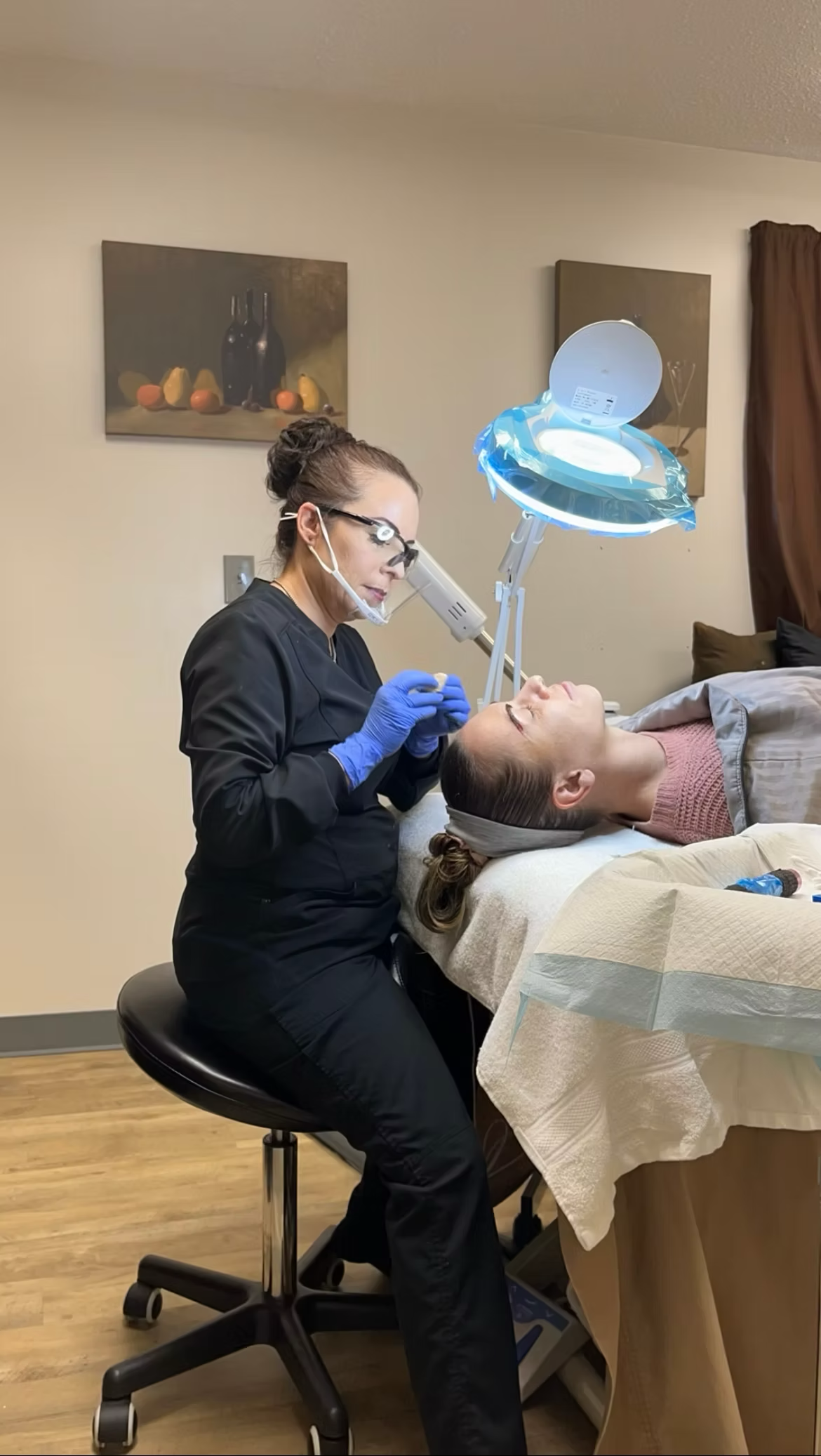 A woman is sitting on a stool while a patient is laying on a bed.