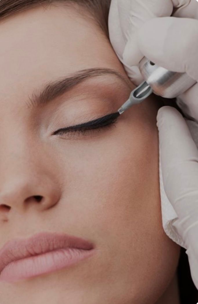 A woman is getting an eyeliner tattoo on her eye.