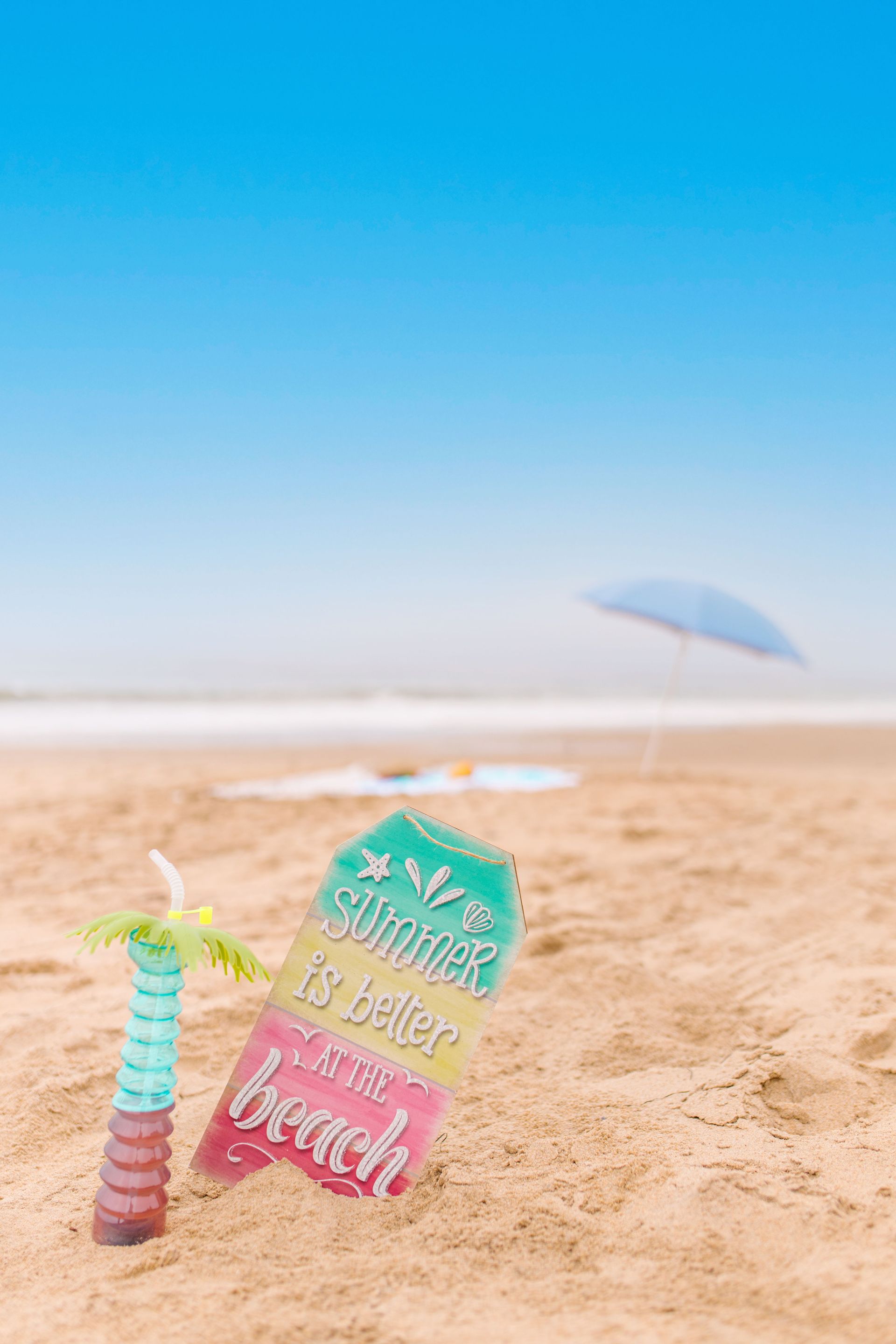 Pastel beach sign and umbrella in sand under a bright blue sky
