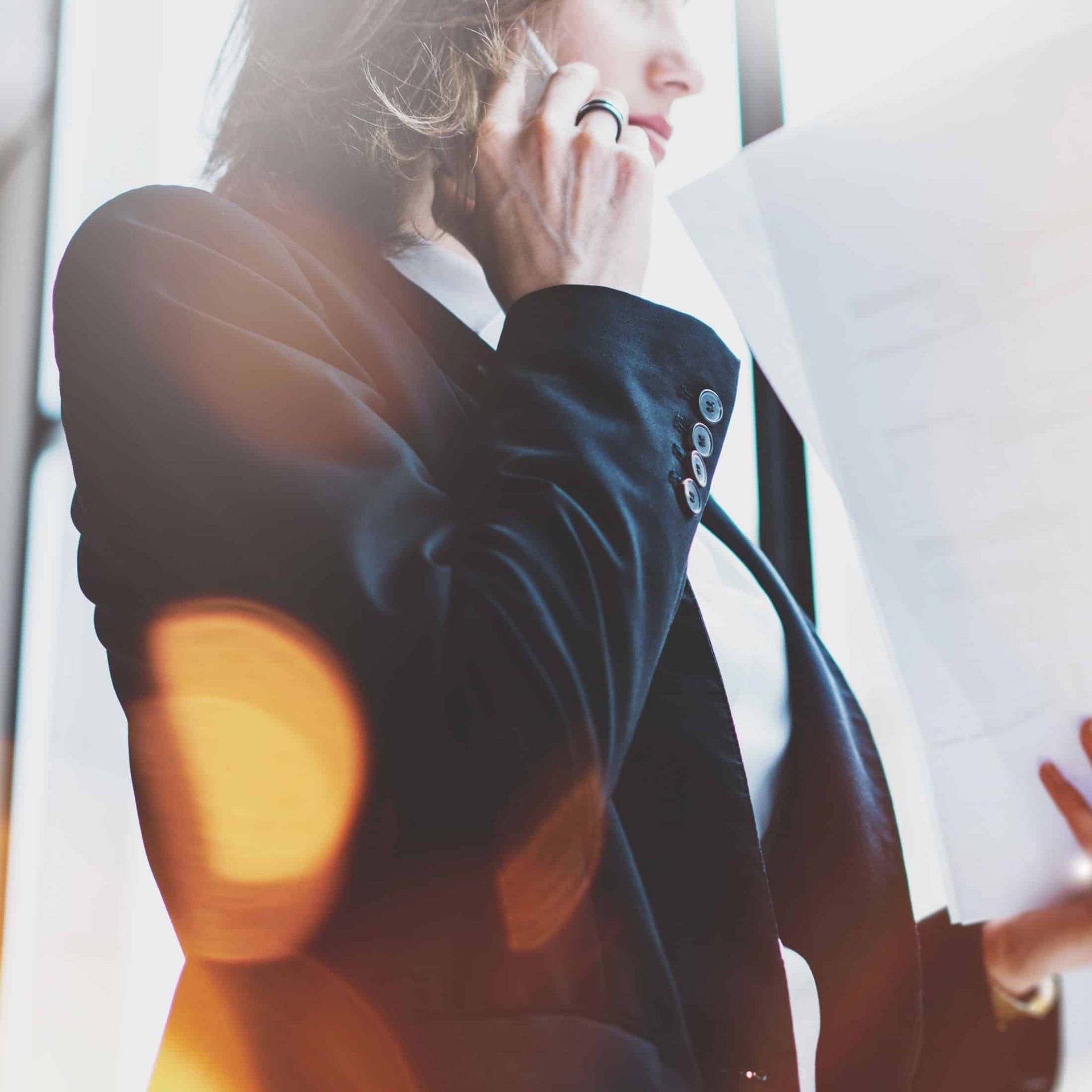 Person in a dark blazer talks on a phone by a bright window