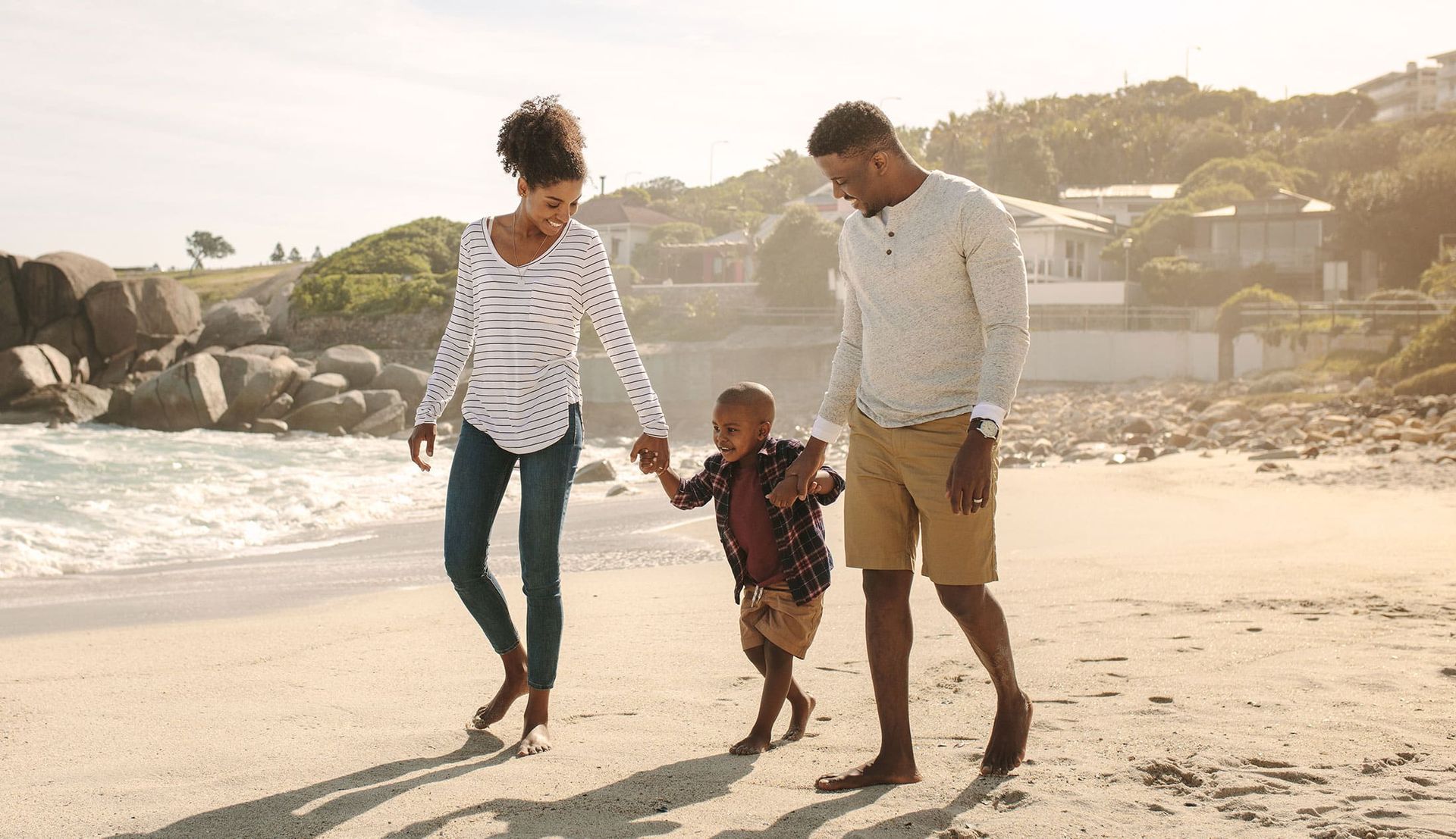 Family walking barefoot along a sunny beach, holding hands near the shoreline