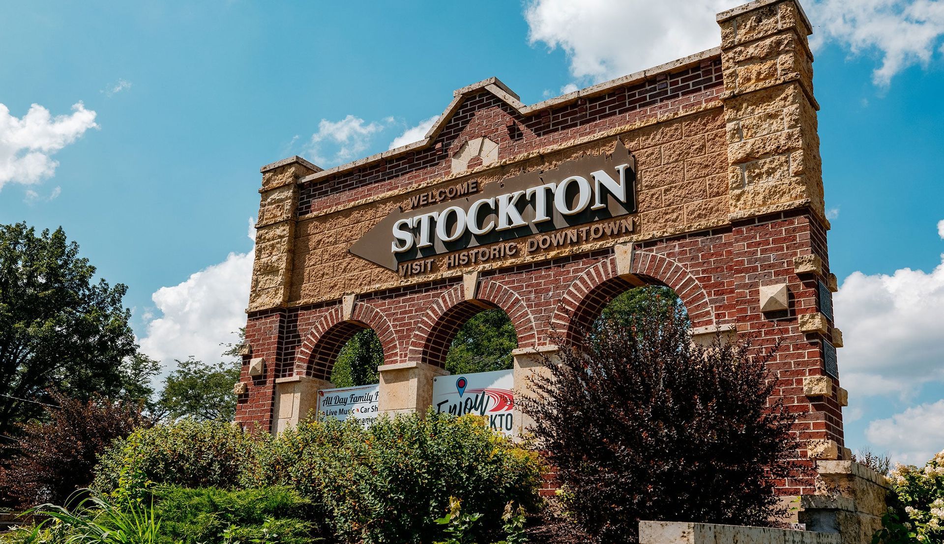 Brick Stockton sign on a historic building facade, framed by trees and blue sky.