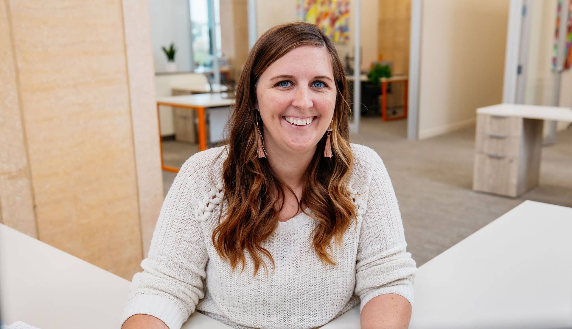 Smiling woman in a white sweater seated in a bright office lounge