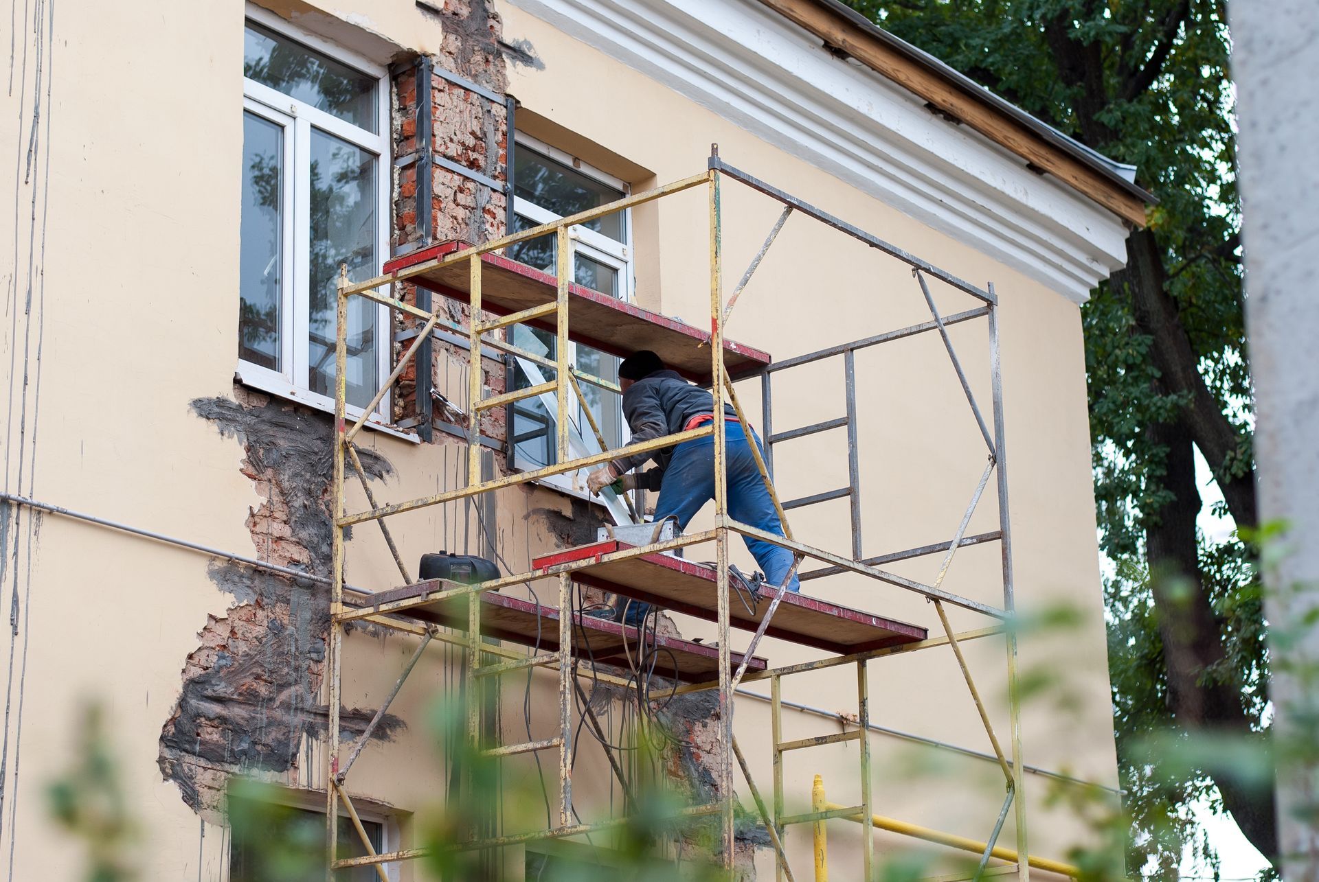 Man on scaffolding repairing building exterior near a window