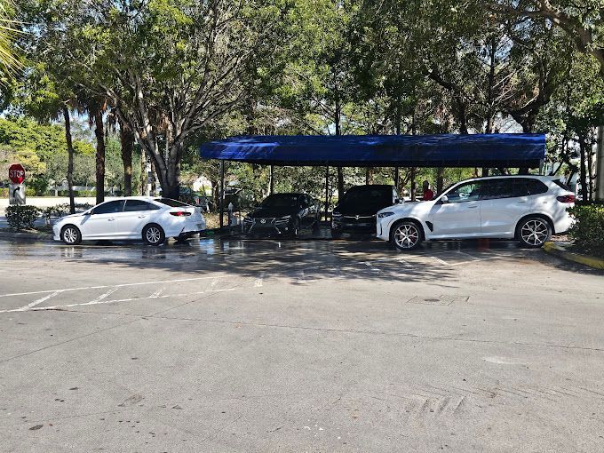 Two white cars are parked under a blue canopy in a parking lot.