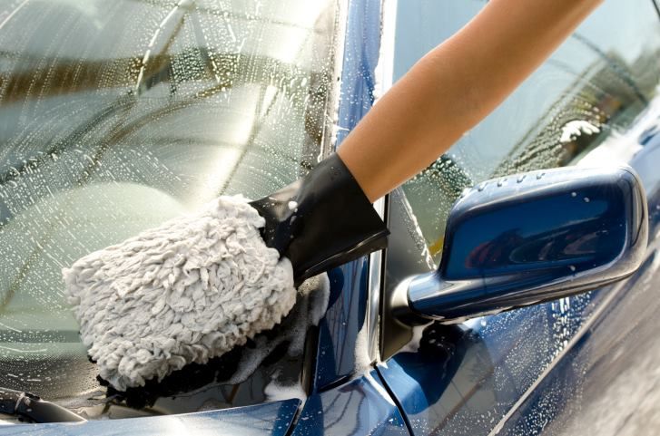 Person washing a blue car windshield with a soapy sponge.