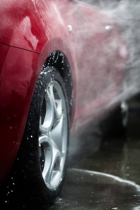 Red car being washed; water spraying on tire and body.