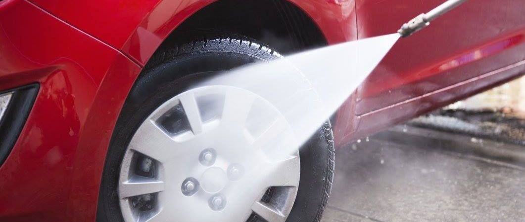 Red car being washed with a high-pressure spray, focusing on a tire.