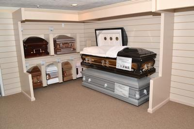 Memorial display with caskets in a beige showroom under a white-beamed ceiling