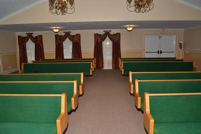 Empty church sanctuary with green pews, red curtains, and a central aisle leading to the front.