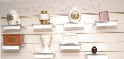Small display of decorative urns and keepsake boxes on floating shelves in a memorial showroom