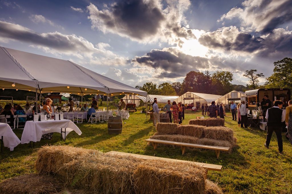 Outdoor event with tents, hay bales, and people; sunny day.