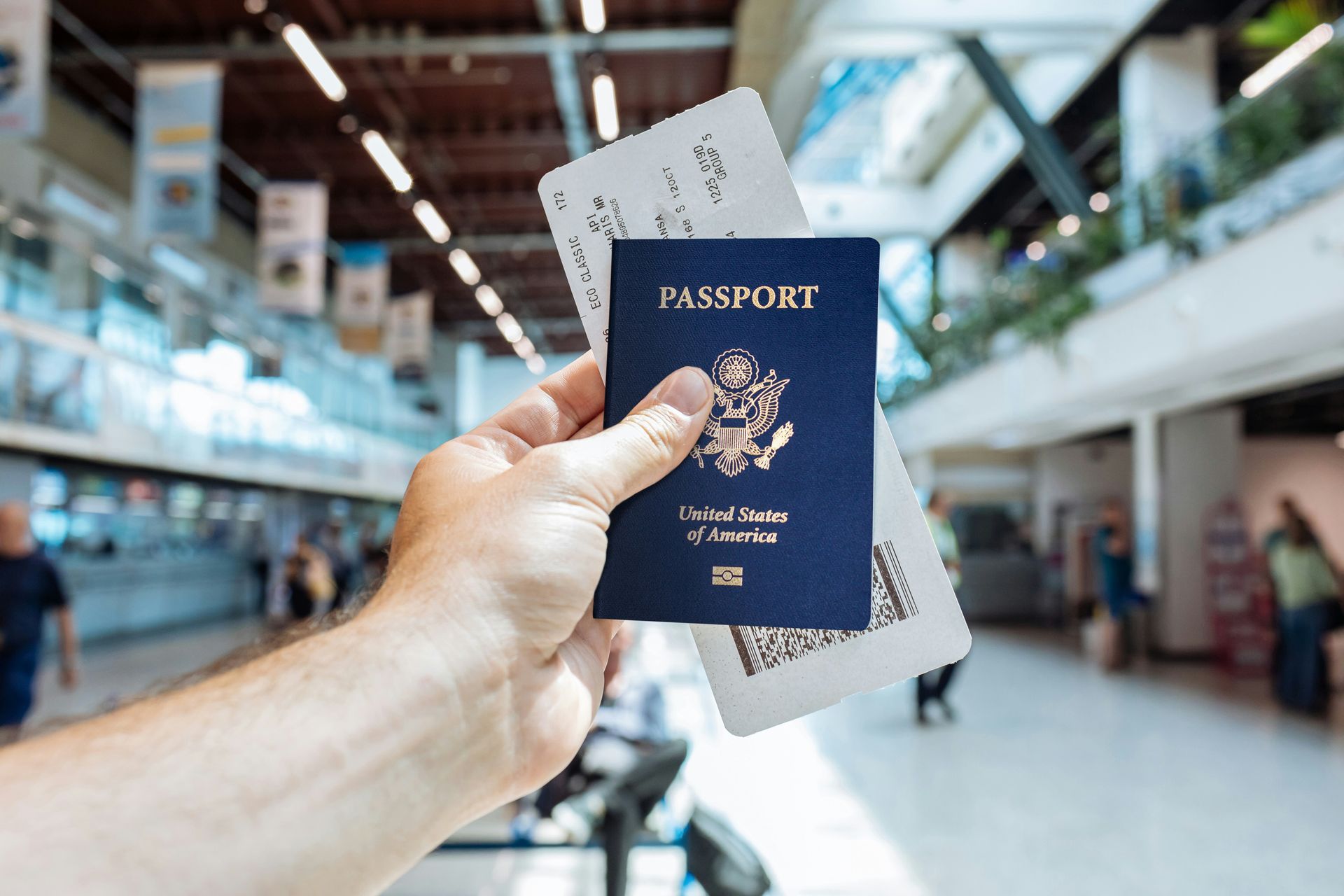 Una mano sostiene un pasaporte azul y una tarjeta de embarque en la terminal de un aeropuerto.