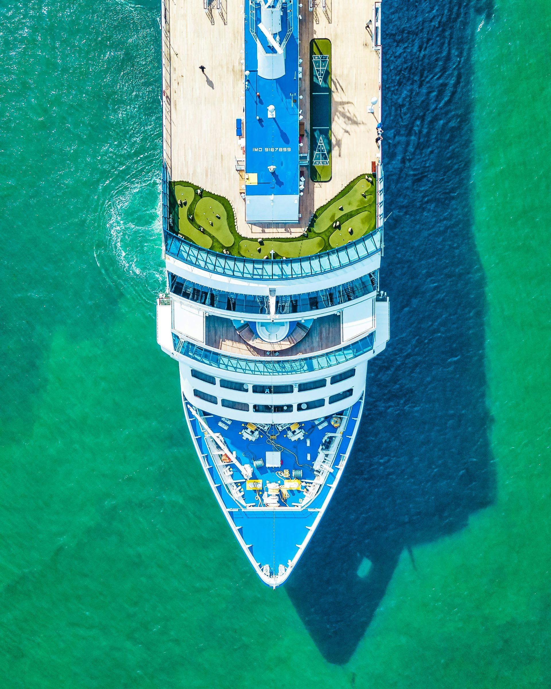 Vista aérea de un crucero azul y blanco en aguas turquesas, atracado junto a un muelle.