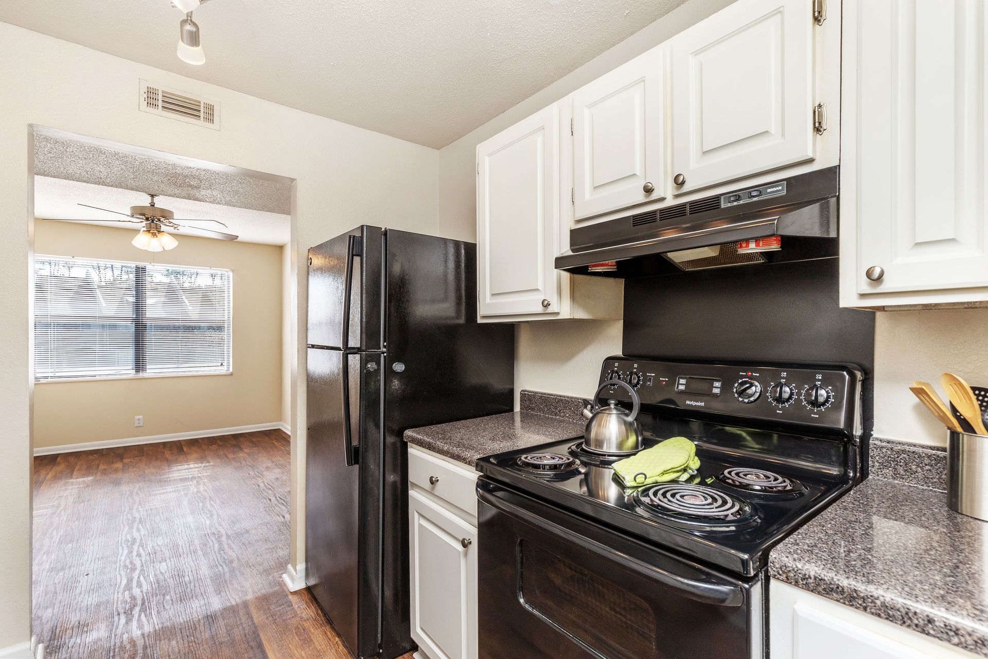A kitchen with white cabinets, black appliances, a granite-look countertop, and a view into an adjacent dining area.