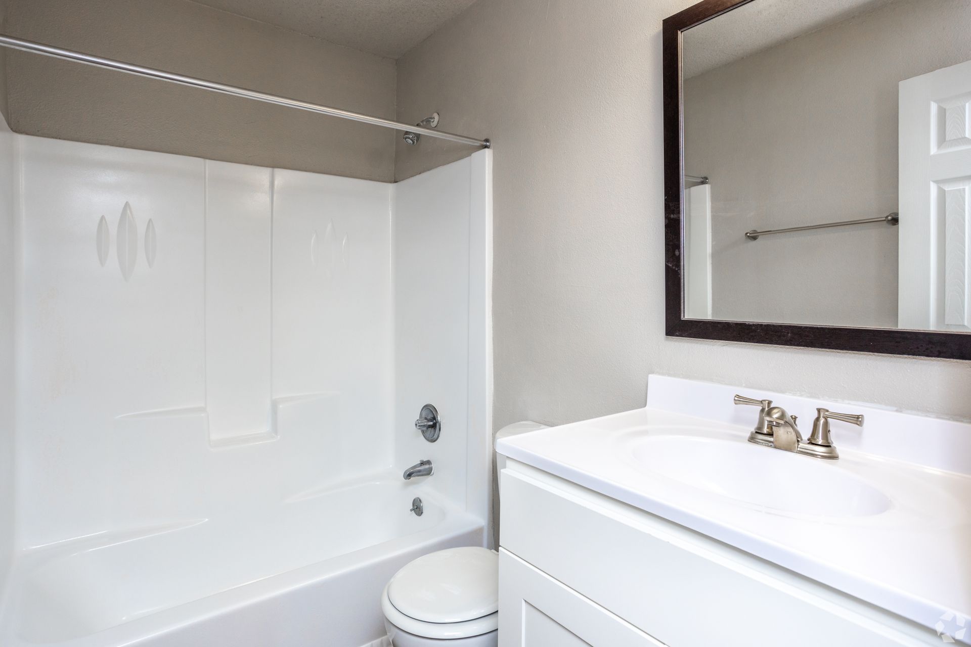 A bright, modern bathroom featuring a white vanity with a sink, a wall mirror, and a white bathtub-shower combo.
