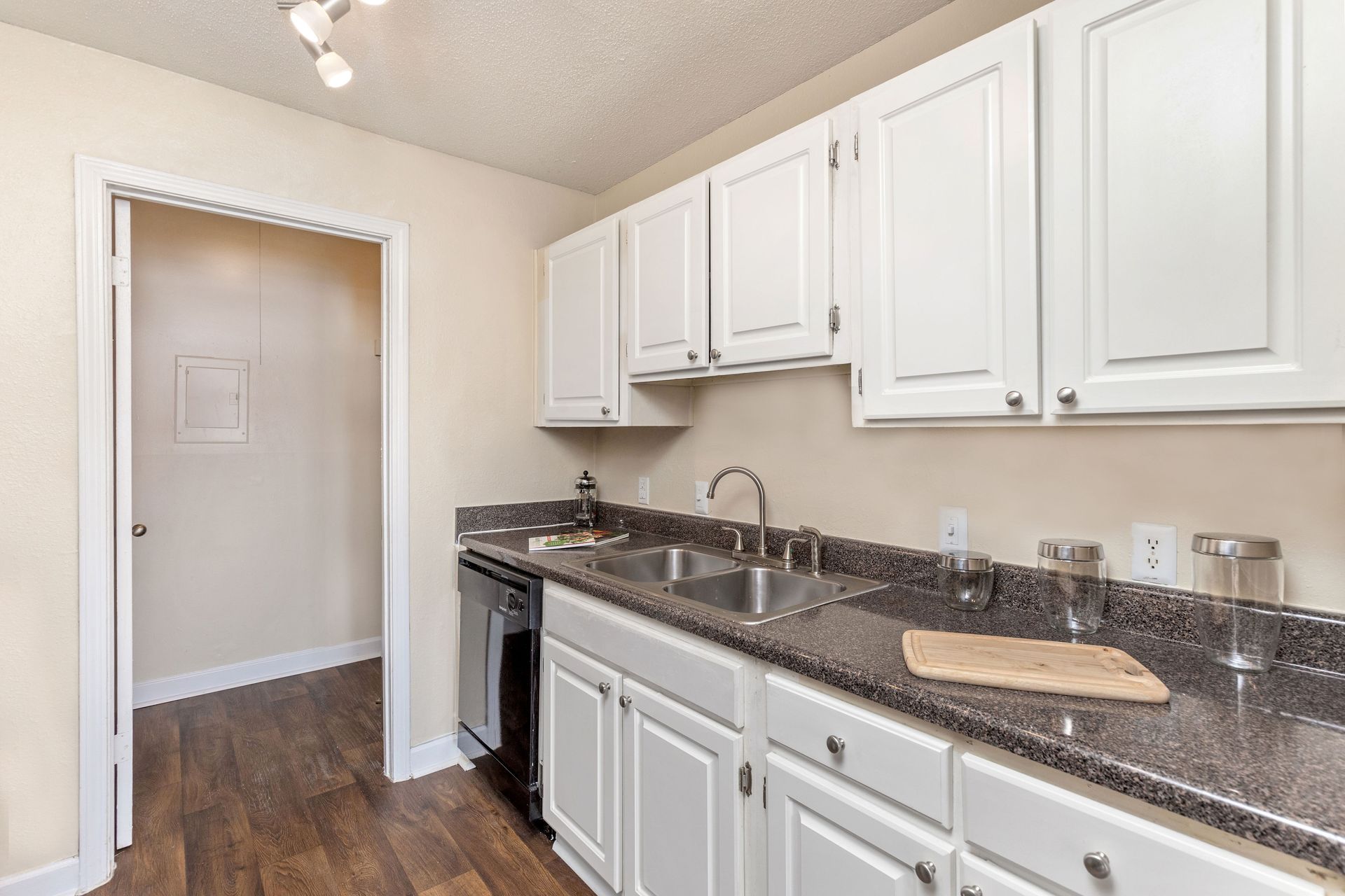 A modern kitchen featuring white cabinets, dark granite countertops, a double sink, and a view into an adjacent room.
