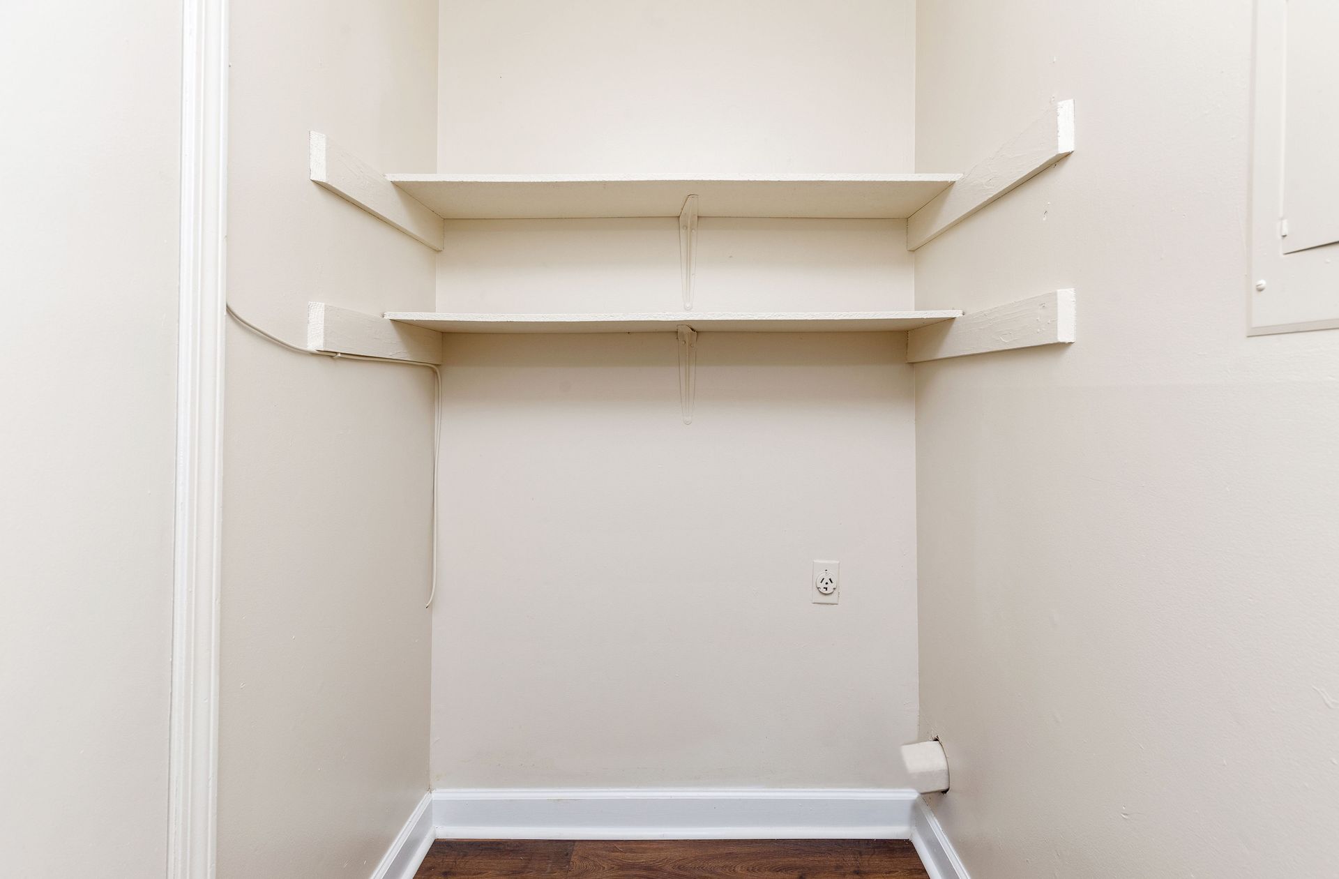 An empty closet alcove with two white wooden shelves mounted on the wall above a small electrical outlet.
