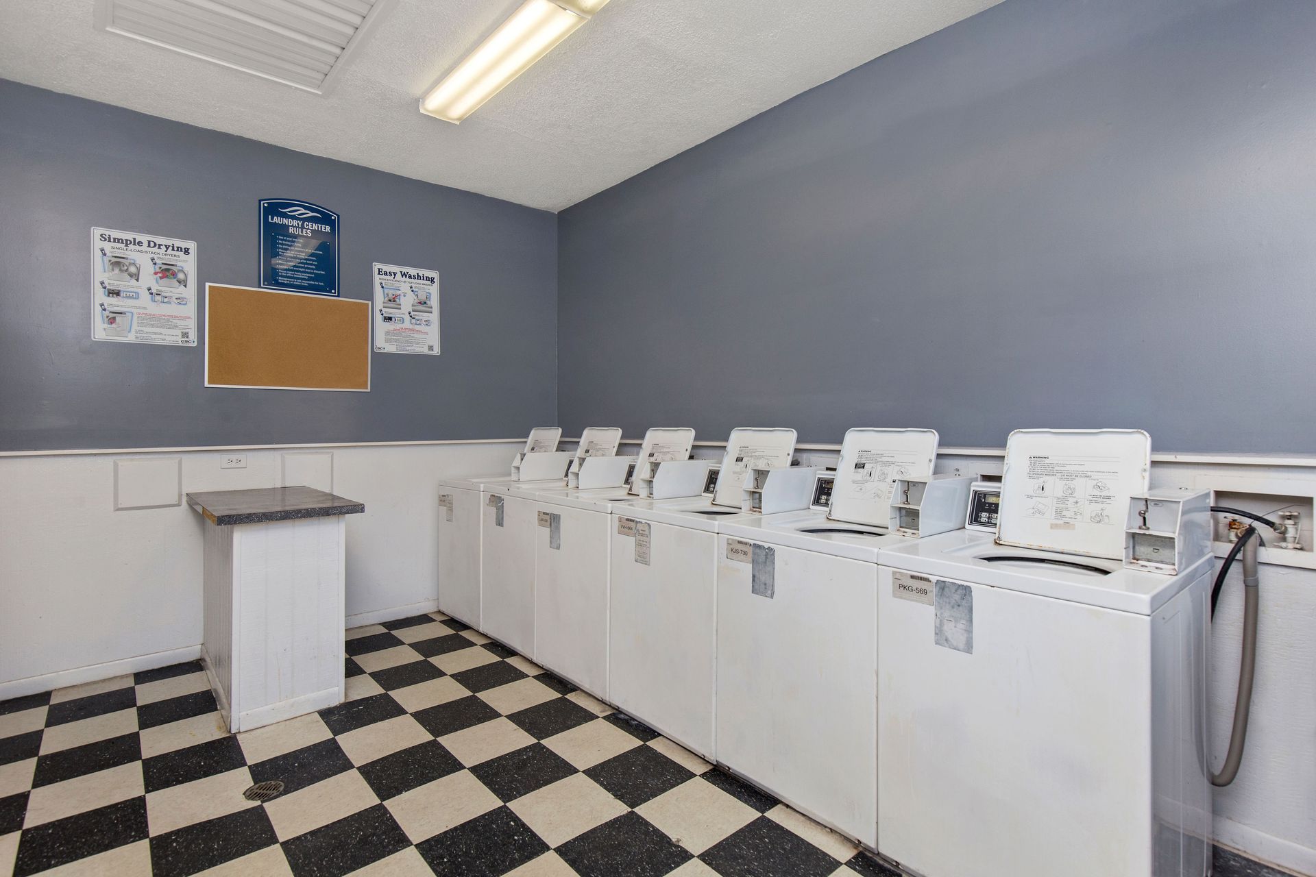 A laundry room with a black-and-white checkered floor, gray walls, and a row of white washing machines.
