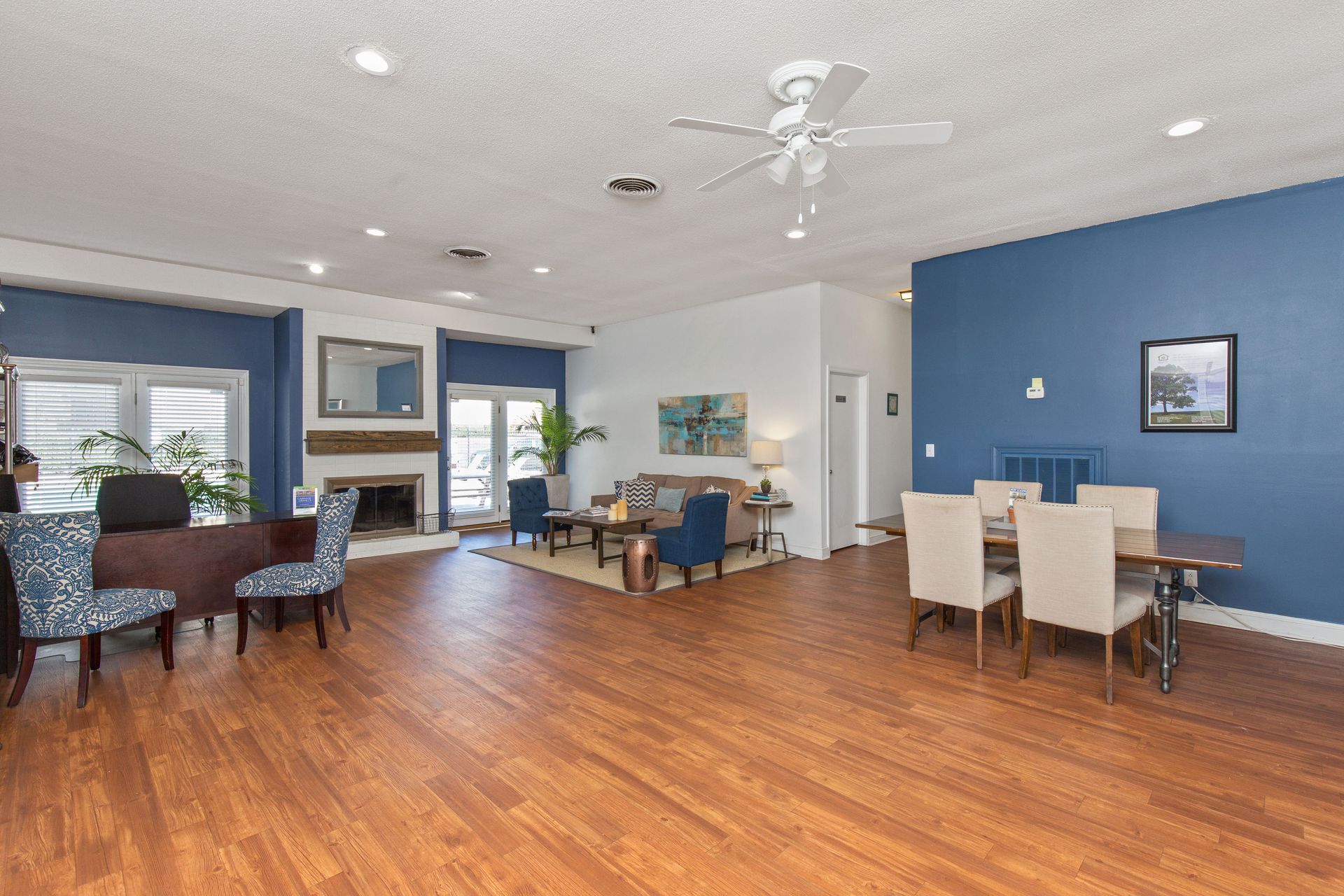 Spacious, modern open-plan living and dining area with blue accent walls, wood floors, and a stone fireplace.