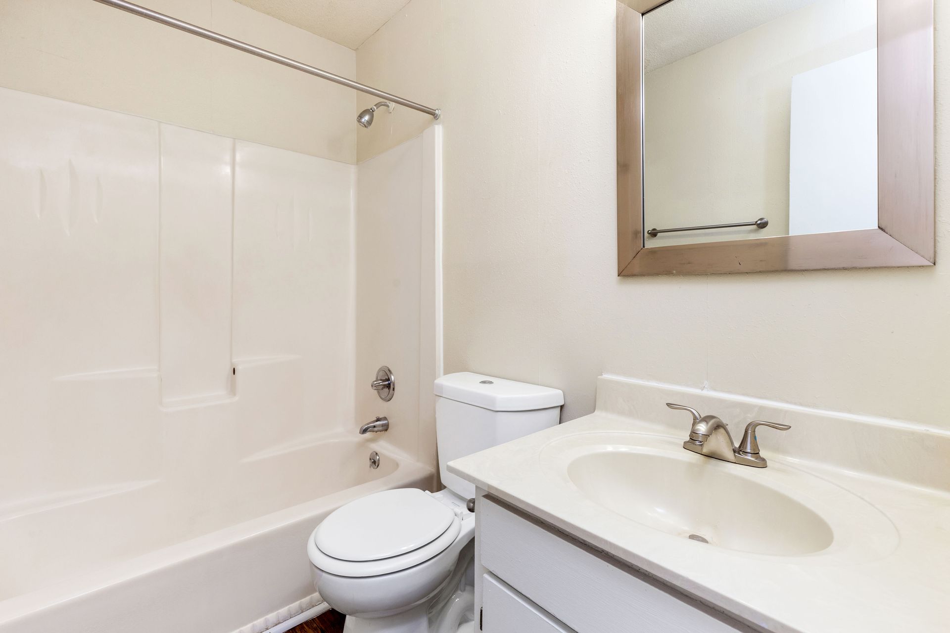 A bright, clean bathroom featuring a white vanity with a single sink, a mirror, and a combined tub and shower unit.