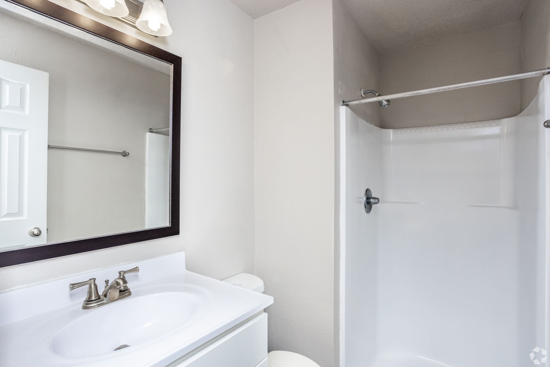 A clean, modern bathroom with a white vanity, a large framed mirror, a toilet, and a white walk-in shower stall.
