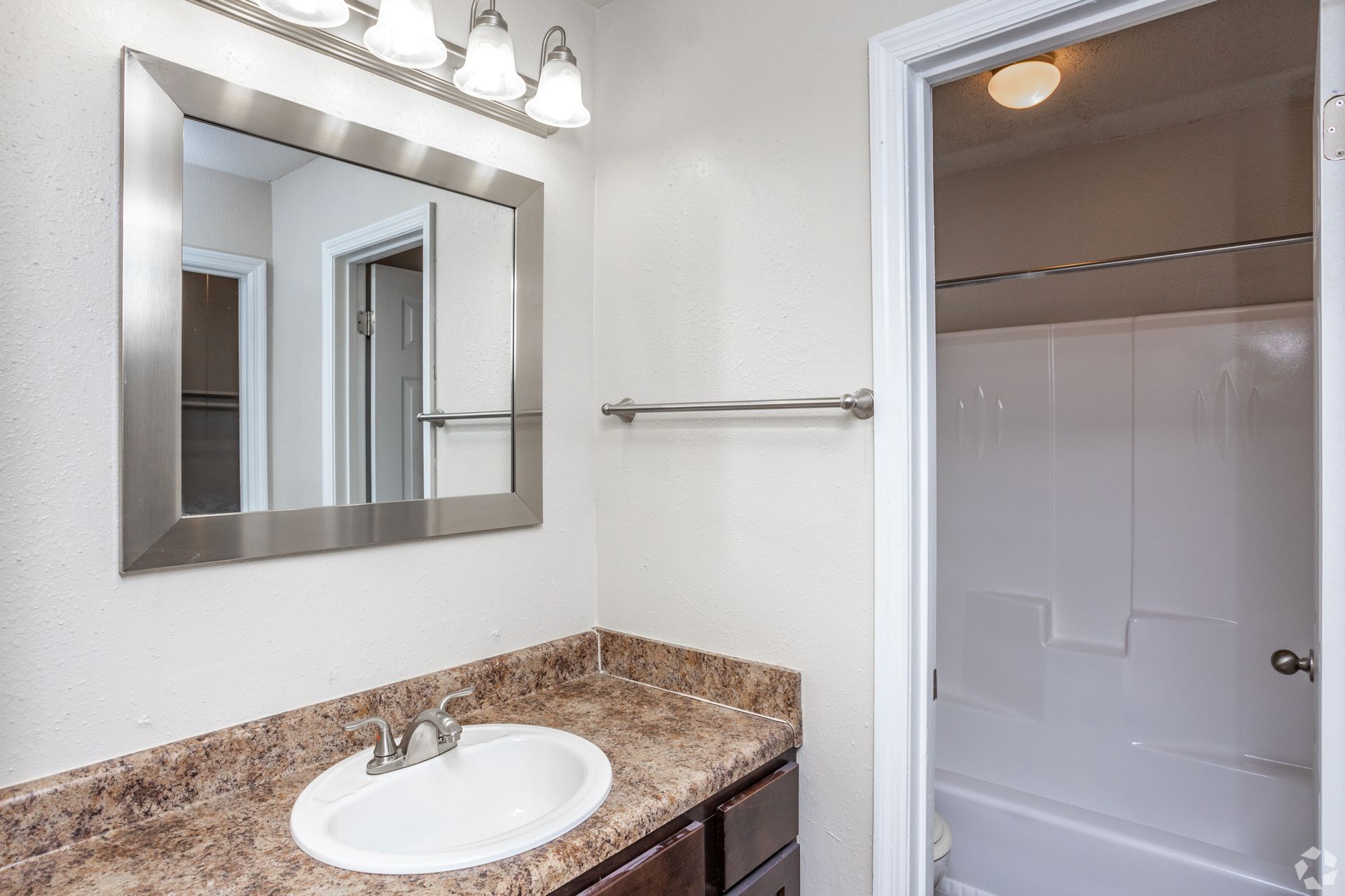A bathroom vanity with a speckled granite countertop, stainless steel mirror, and an adjacent shower stall.