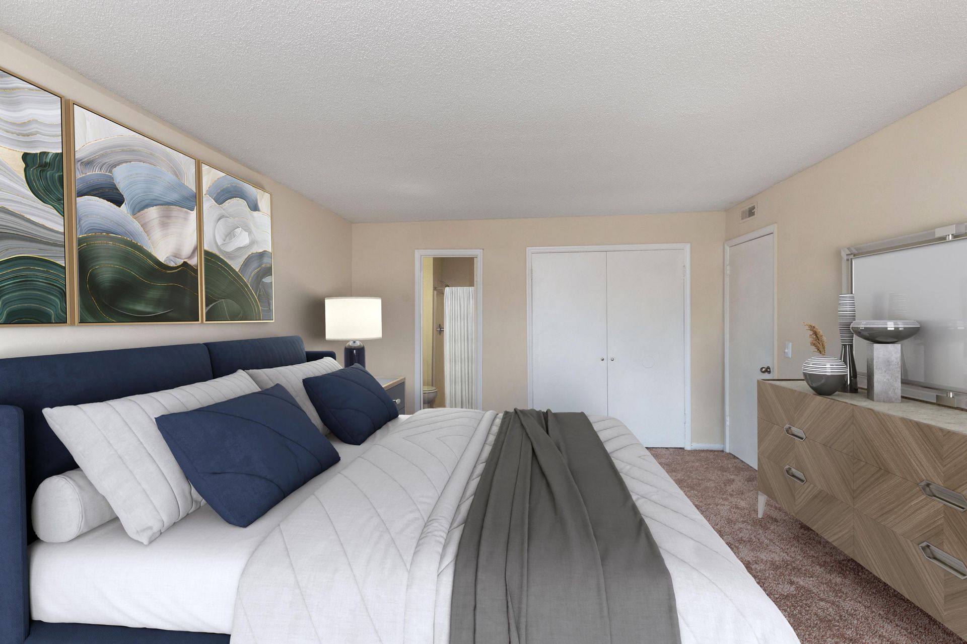 A bedroom with a navy blue upholstered bed, grey bedding, wooden dresser, and artwork on a beige wall.