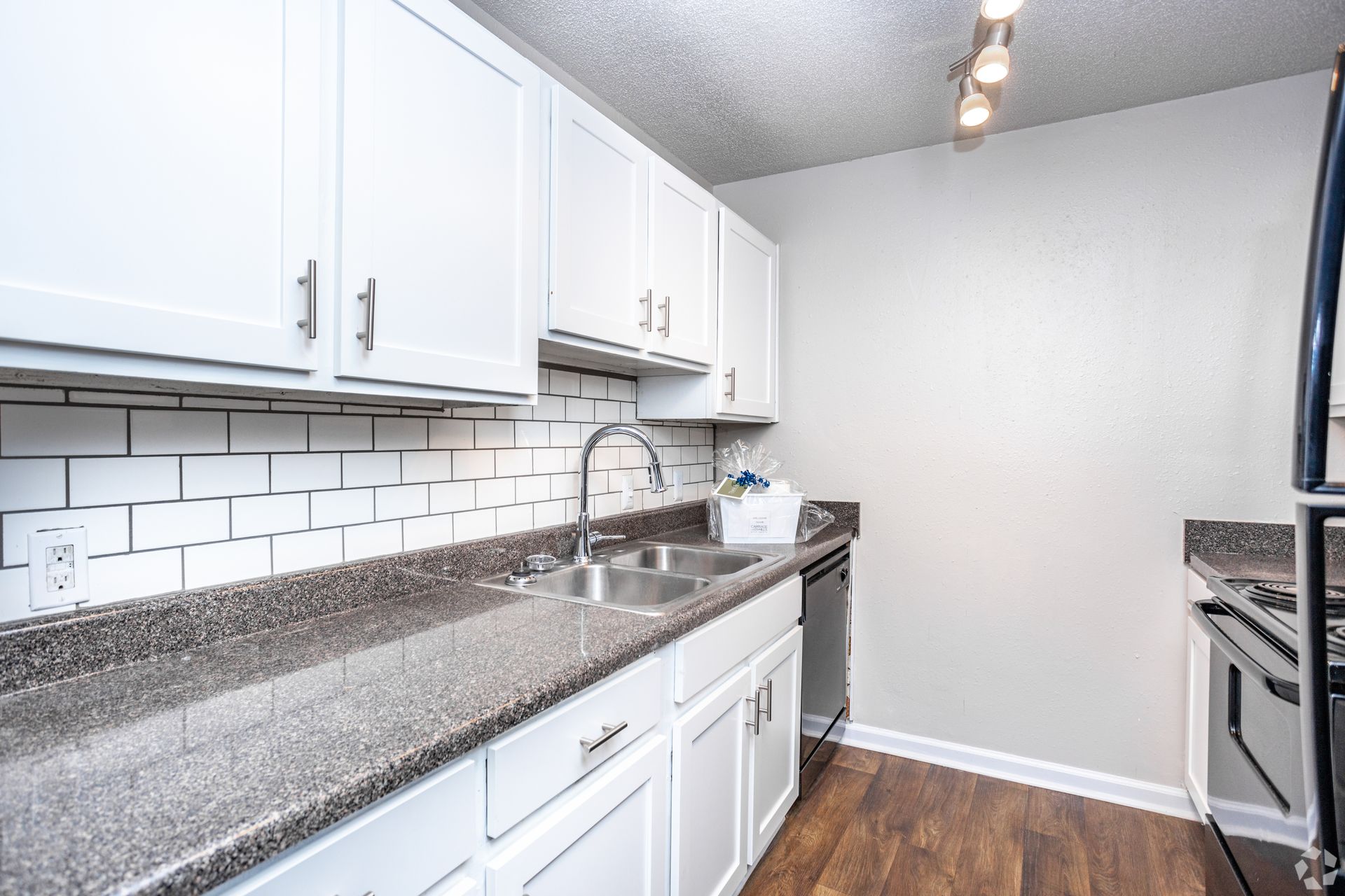 A bright, modern kitchen featuring white cabinets, subway tile backsplash, speckled countertops, and wood-look flooring.