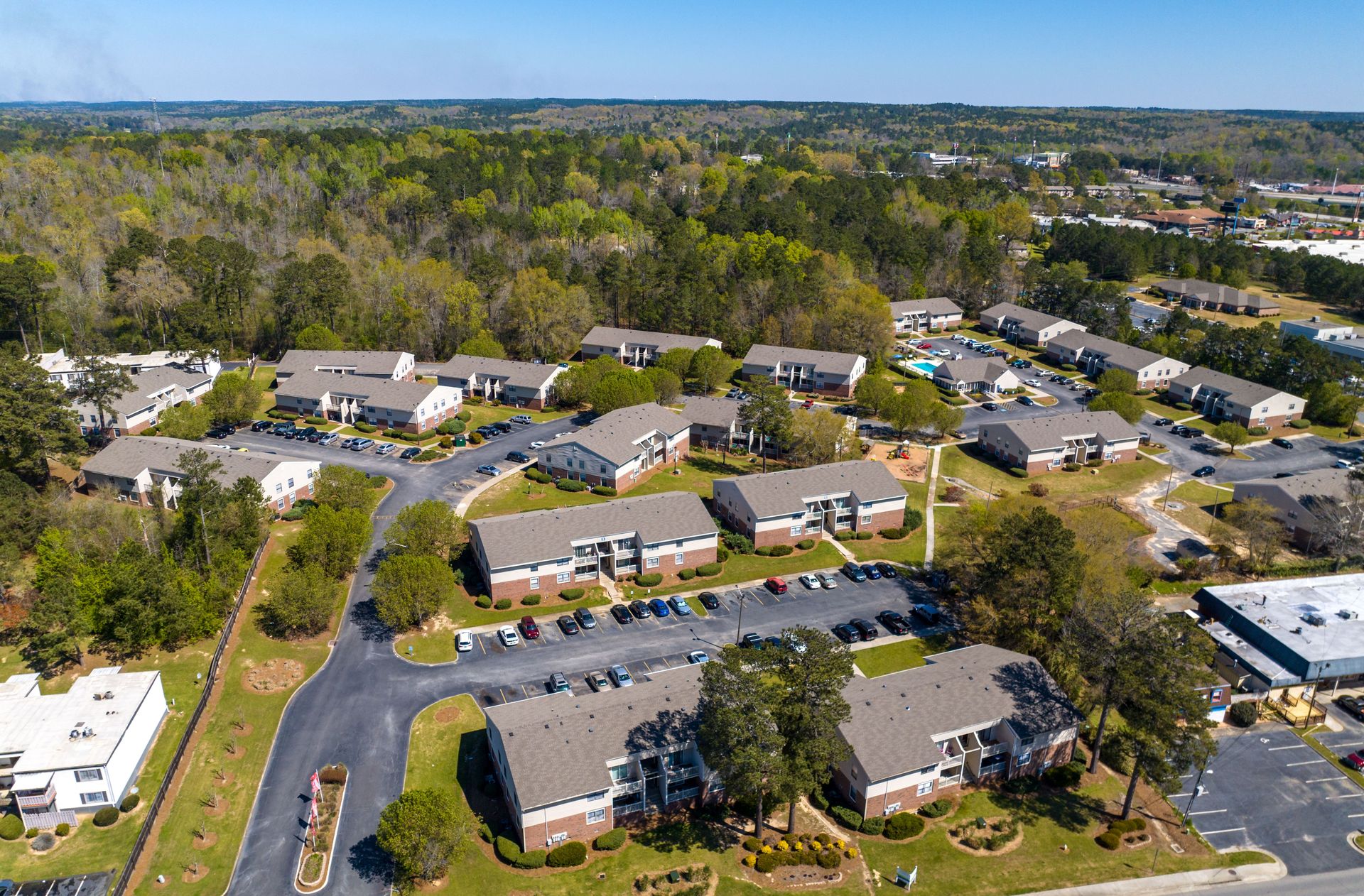 An aerial view of a multi-building apartment complex with parking lots nestled among trees on a sunny day.