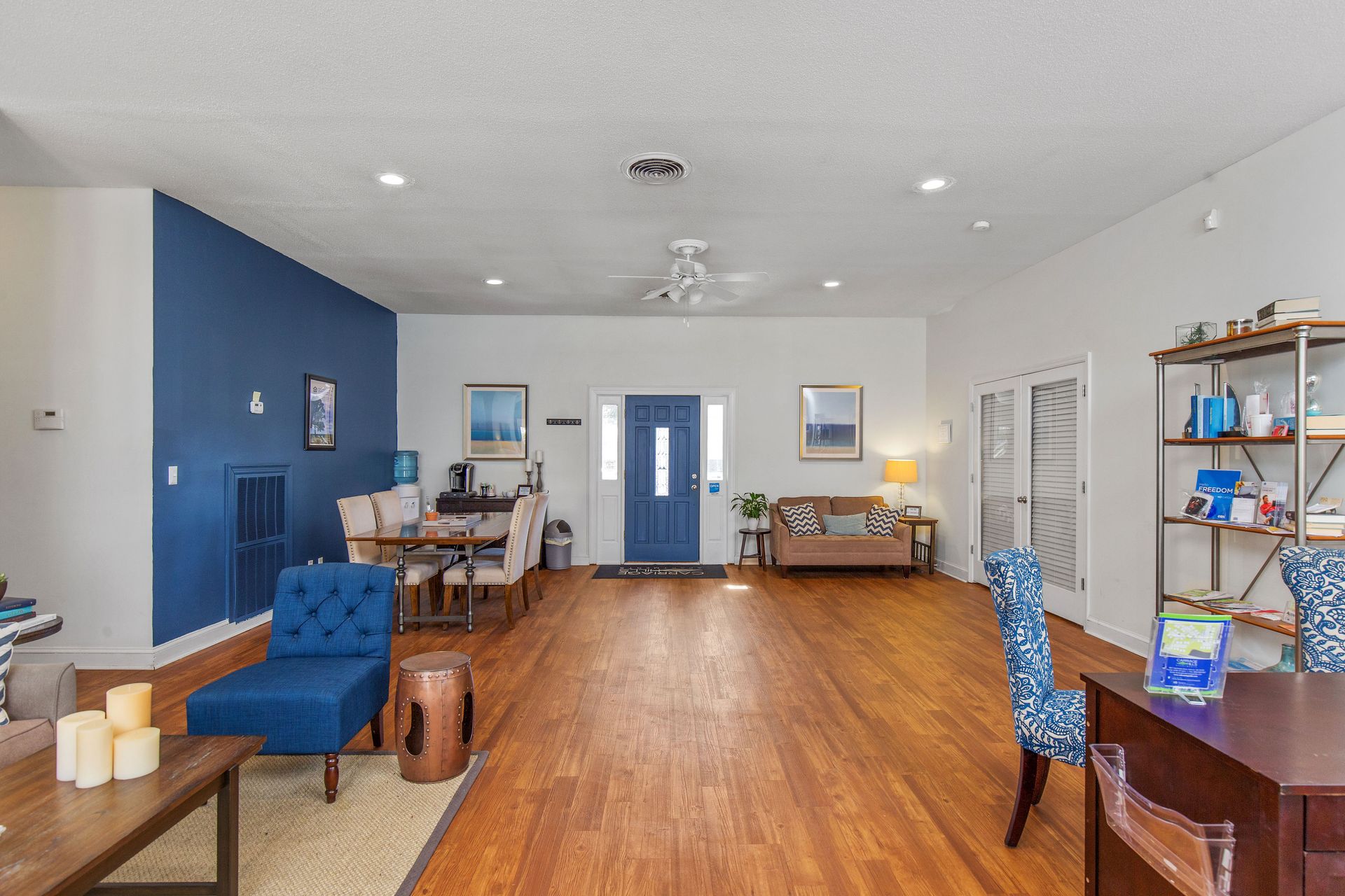 Spacious room with wood floors, a blue accent wall, blue armchair, dining set, and an entrance with a blue door.