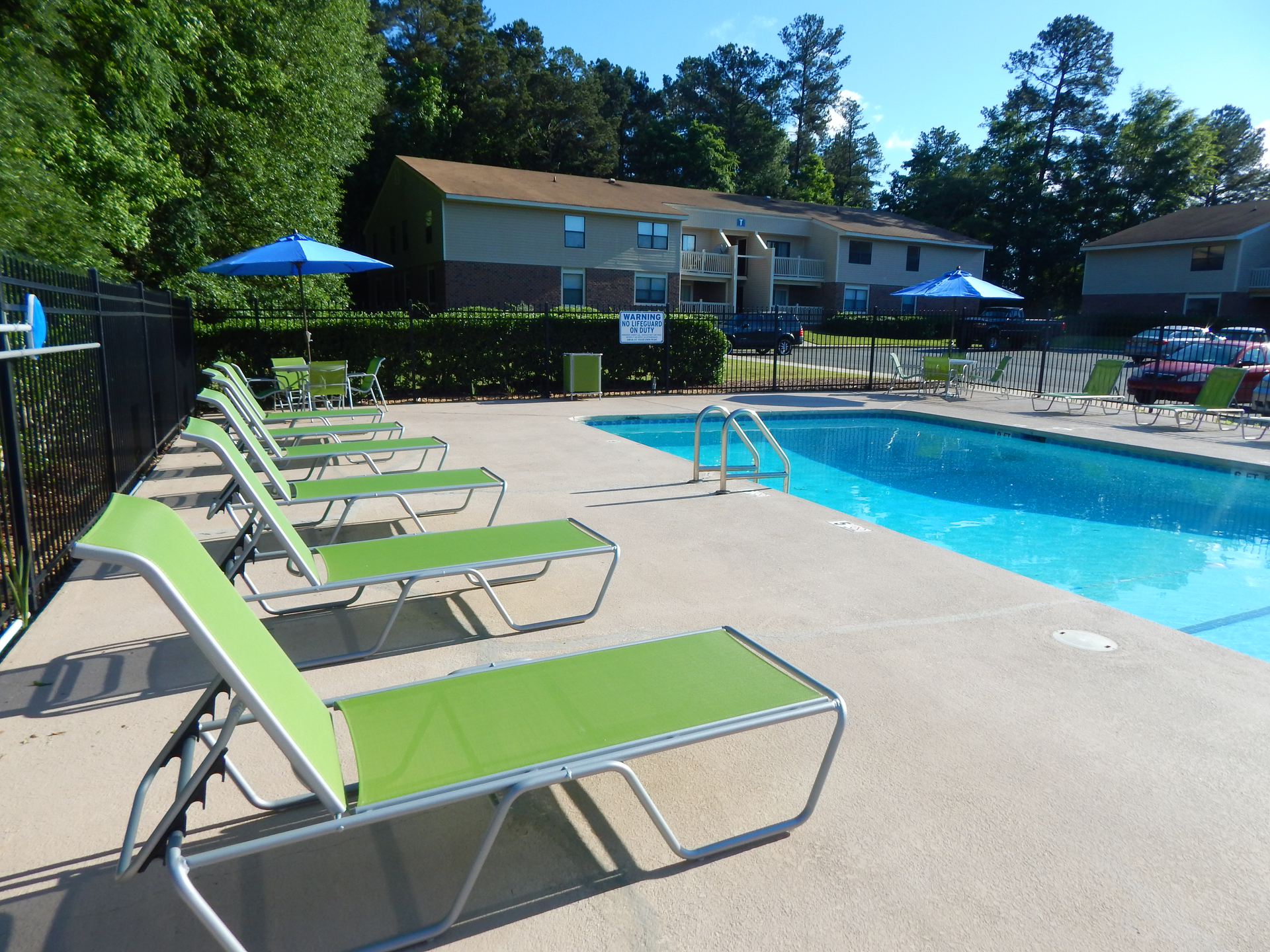 A bright blue swimming pool with lime green lounge chairs on a concrete deck, next to an apartment building.