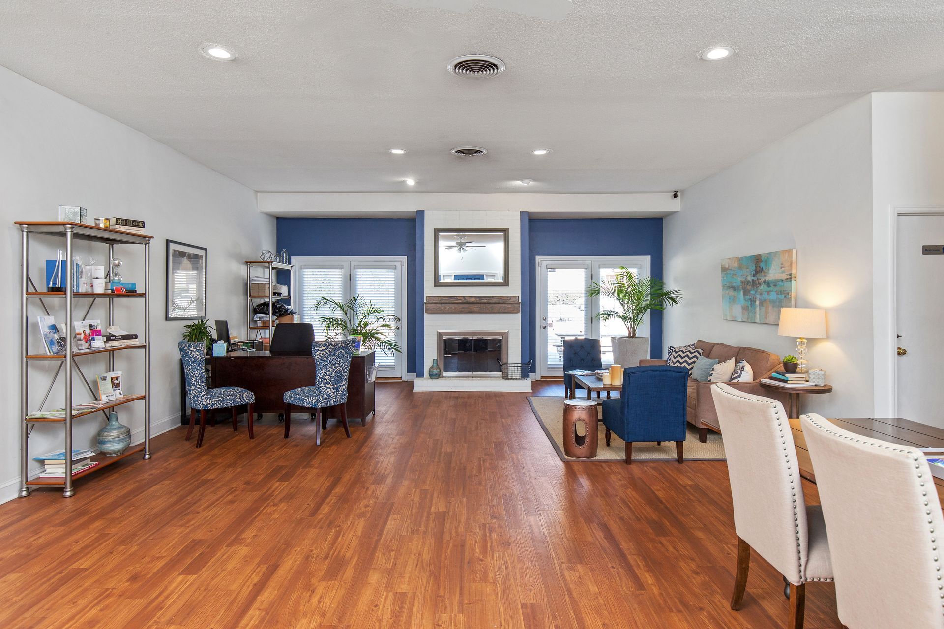 Open-concept living room and office space with wood floors, blue accent walls, a central fireplace, and neutral seating.